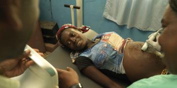 A pregnant woman lies on a bed and smiles as she looks at the screen of her ultrasound scan