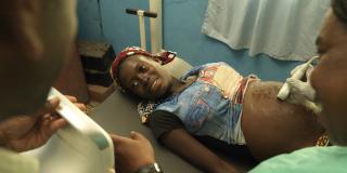 A pregnant woman lies on a bed and smiles as she looks at the screen of her ultrasound scan