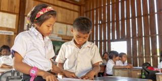 Two young schoolchildren stand at their desk and study together from a textbook