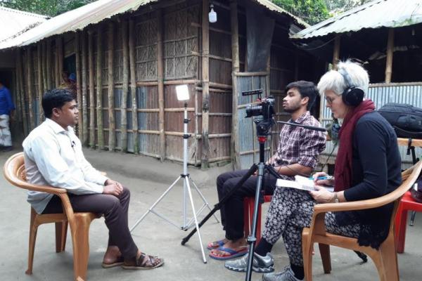 Three people sat on chairs. Two are filming and interviewing the other. 