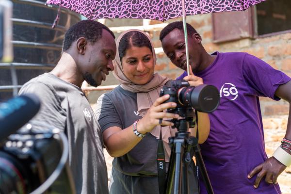 two boys stood either side of a female volunteer who is holding a video camera and recording