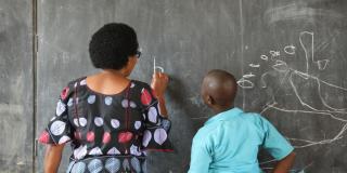 Woman instructs child at chalkboard. Rwanda