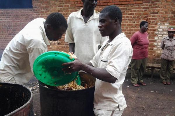 Three male prisoners work at a large drum, preparing grow bags for mushrooms